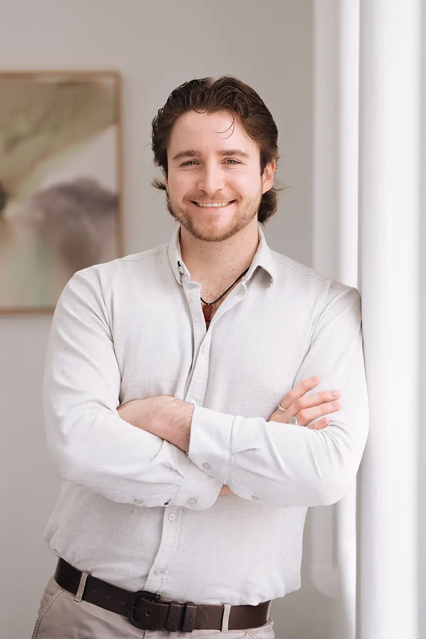 Harry_Dickenson Harry Dickenson, Accountant, wearing a white collared shirt, smiling while leaning against a wall of a light-filled, elegant room