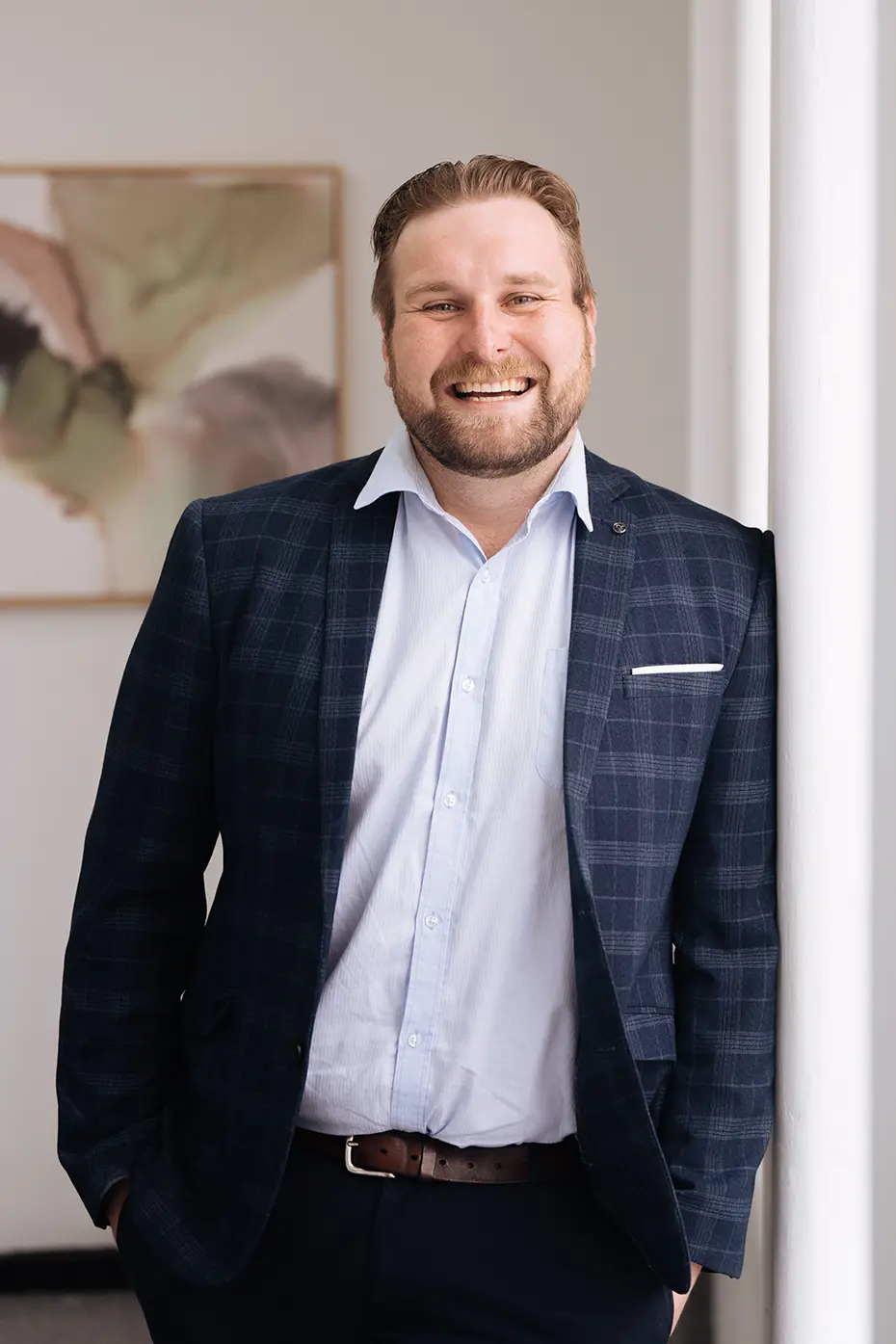 Jim_Shepherd Jim Shepherd, Senior Accountant, wearing a suit, smiling while leaning against a wall of a light-filled, elegant room